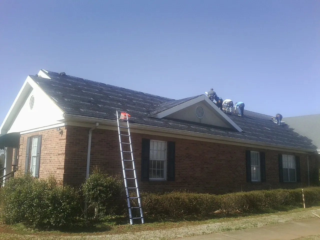 Crew tearing shingles off a brick ranch roof with a ladder set — Metal Roof Repair work by our crew in Homerville