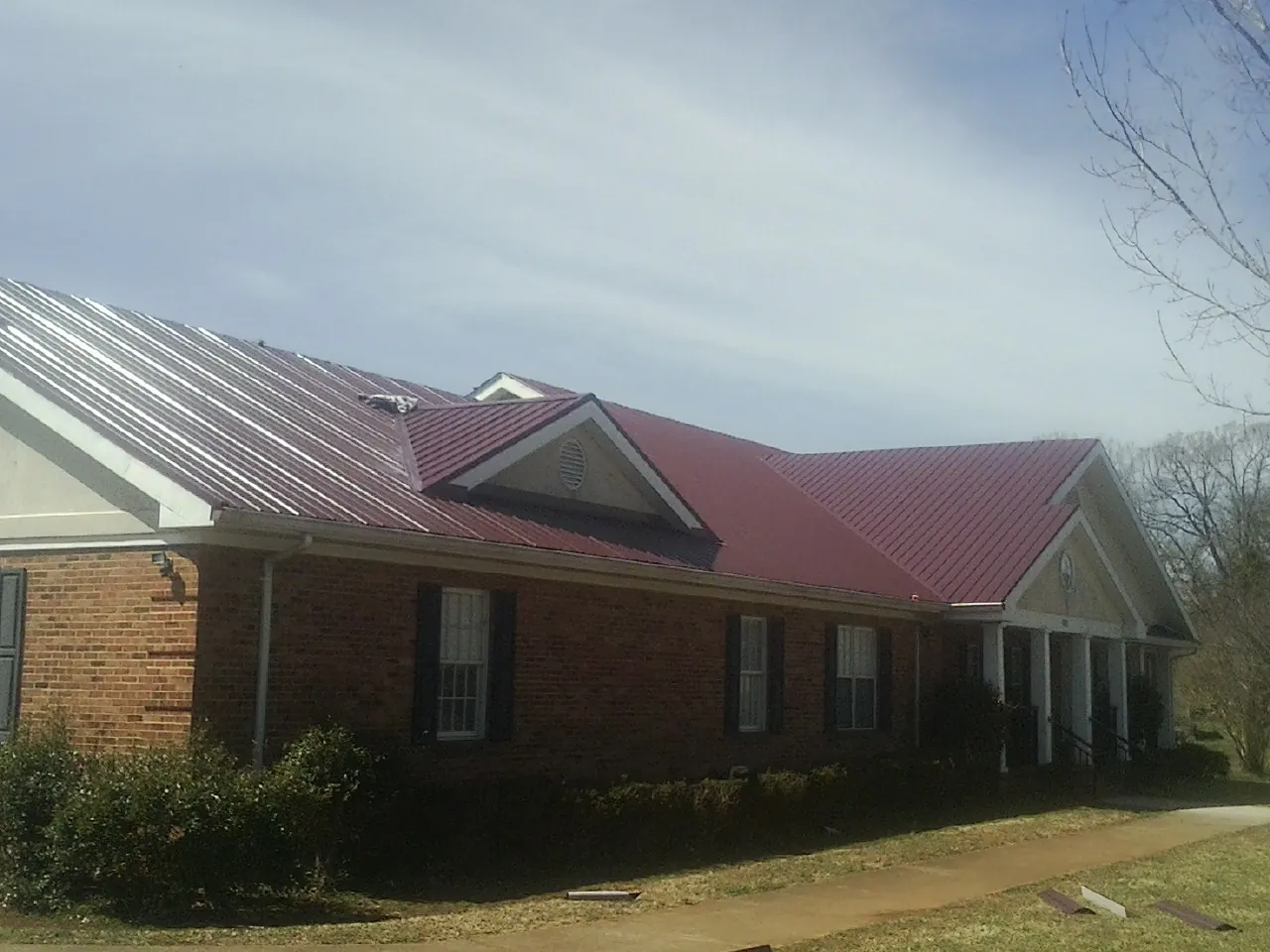 Red metal roof with gabled entries on a long brick building, from a Hail Damage Roof Repair job in Homerville
