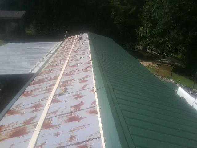 Old rusted panels beside newly installed green metal roofing — Wind Damage Roof Repair by Roofing Brothers in Homerville